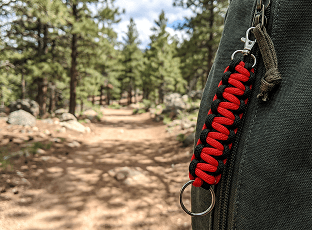 Red paracord zipper pull on a pack along a forest trail